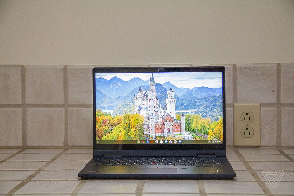 Chromebook Lenovo ThinkPad C13 Yoga widziany z przodu na blacie kafelkowym.  Ekran wyświetla biały zamek otoczony drzewami z górami w tle.